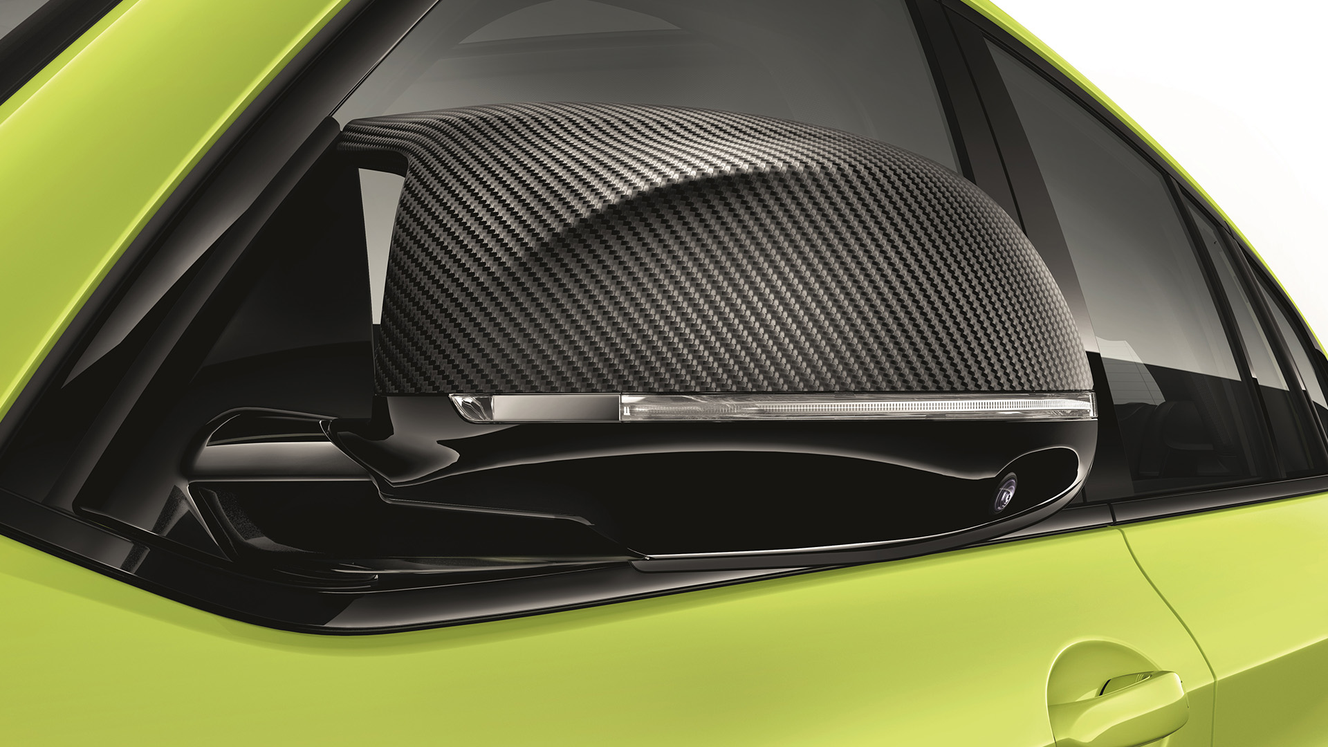 Close-up of a car's side mirror with a carbon fiber cover on a bright green vehicle.