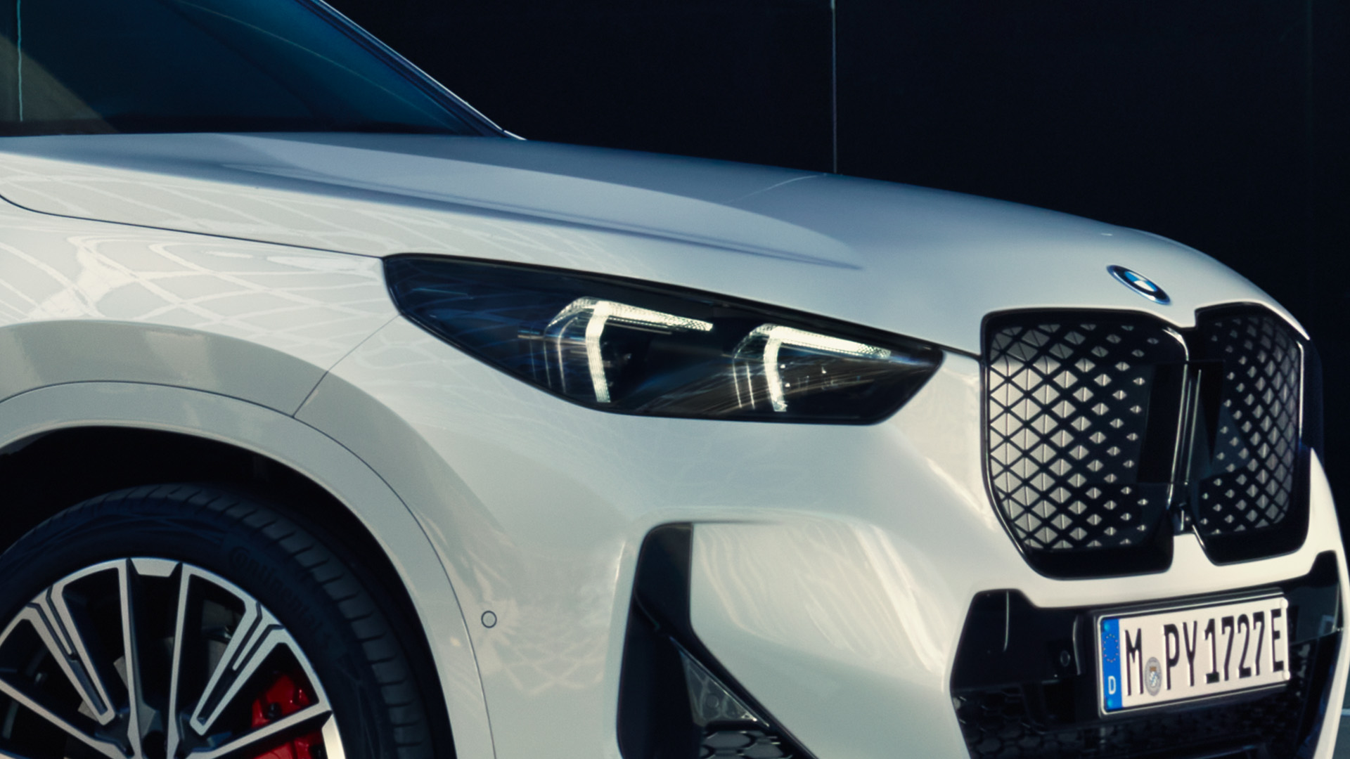 Close-up of the front left side of a white BMW car, showing the headlight, grille, and part of the wheel with red brake calipers. 