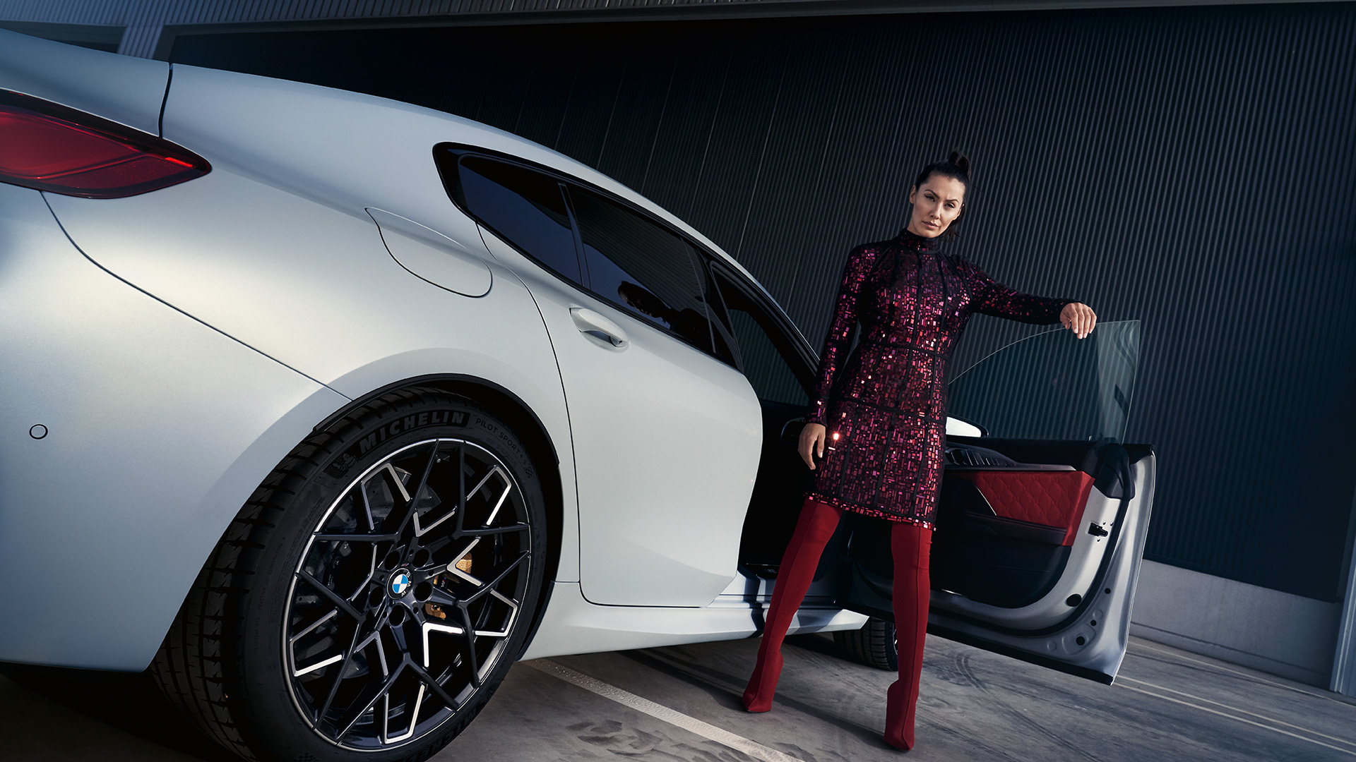 A person standing next to an open door of a white BMW car in a modern garage.