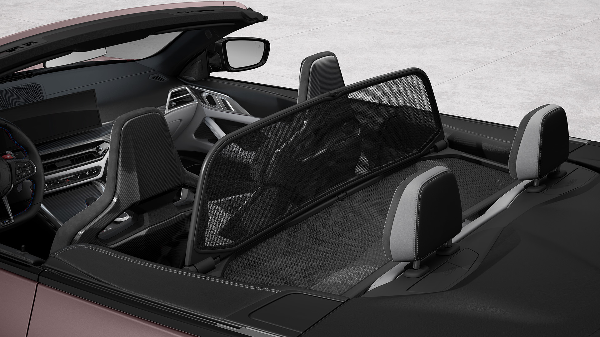 Interior view of a convertible car with the top down, showing the front seats, dashboard, and a mesh wind deflector behind the seats.