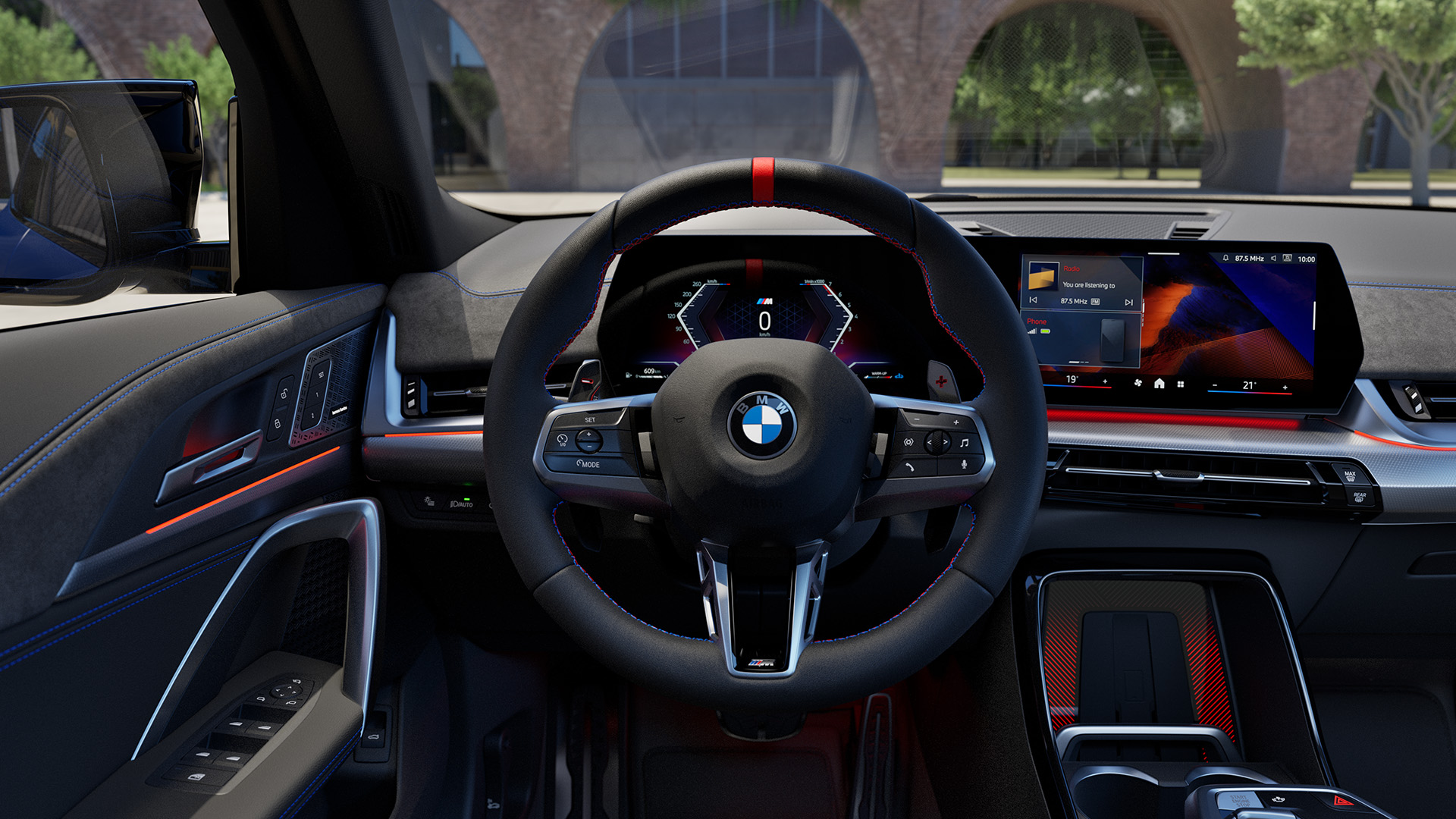 Interior view of a modern BMW car showing the steering wheel, dashboard, and infotainment system with a scenic outdoor background.