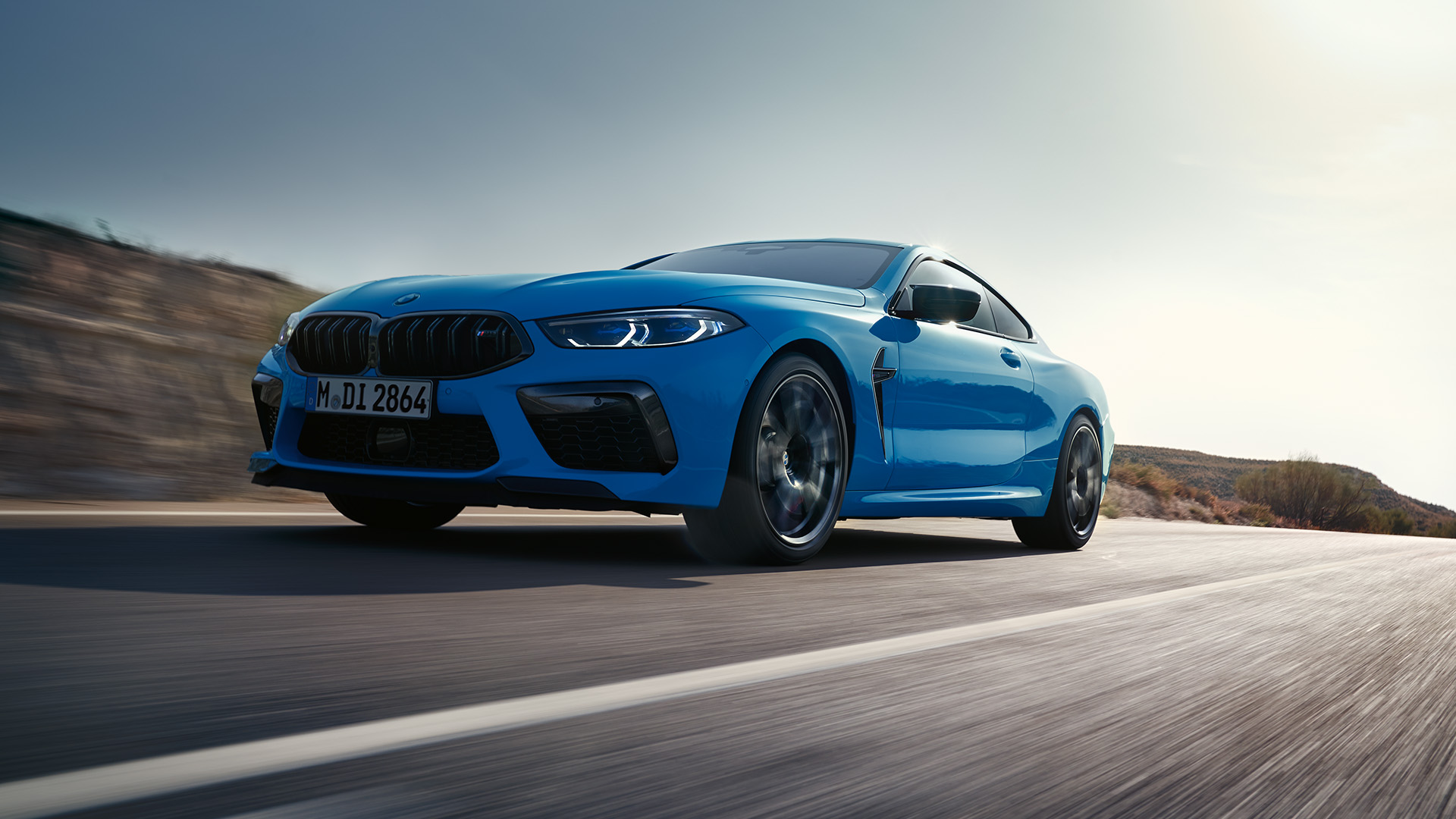 Blue BMW car driving on an open road under a clear sky, captured from a low angle to highlight its speed and sleek design.