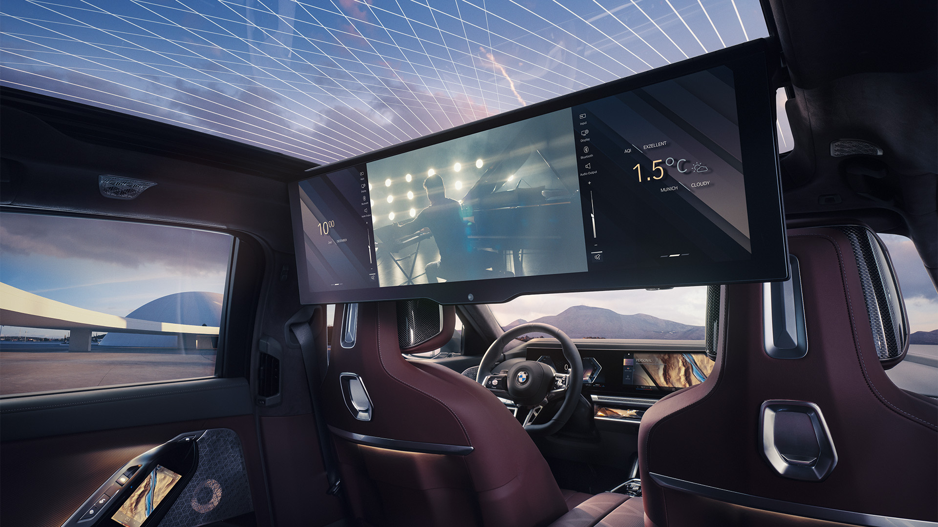 Interior of a luxury BMW car with a panoramic sunroof, featuring a large digital screen mounted behind the front seats displaying 1.5°C temperature and an image of a person playing the piano.