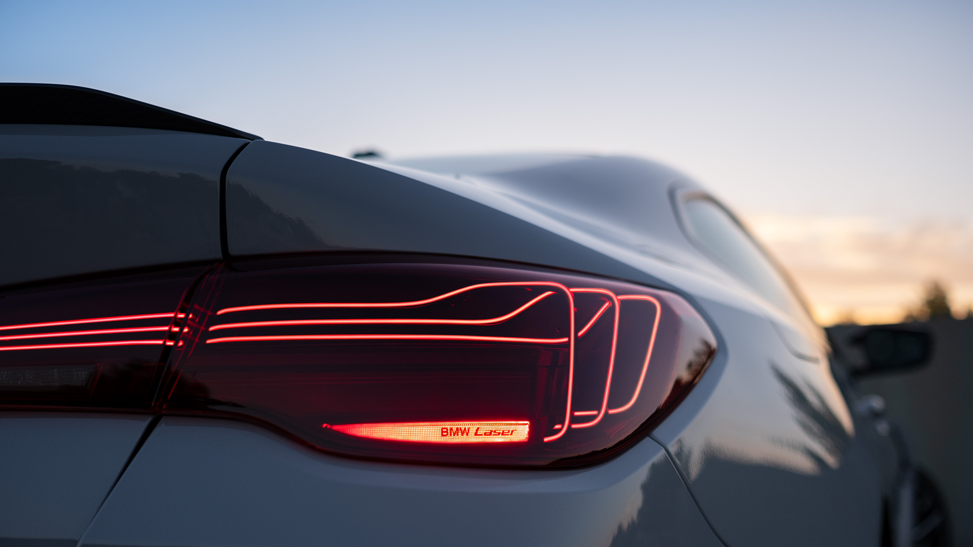 Close-up of the rear right breaklight of a BMW car at dusk, with the text 'BMW Laser' illuminated in the breaklight in red.
