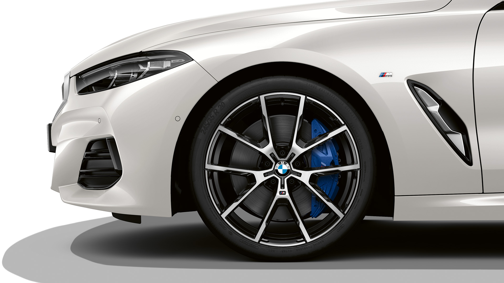 Front side view of a white BMW car showing the front wheel, headlight, and part of the front bumper.