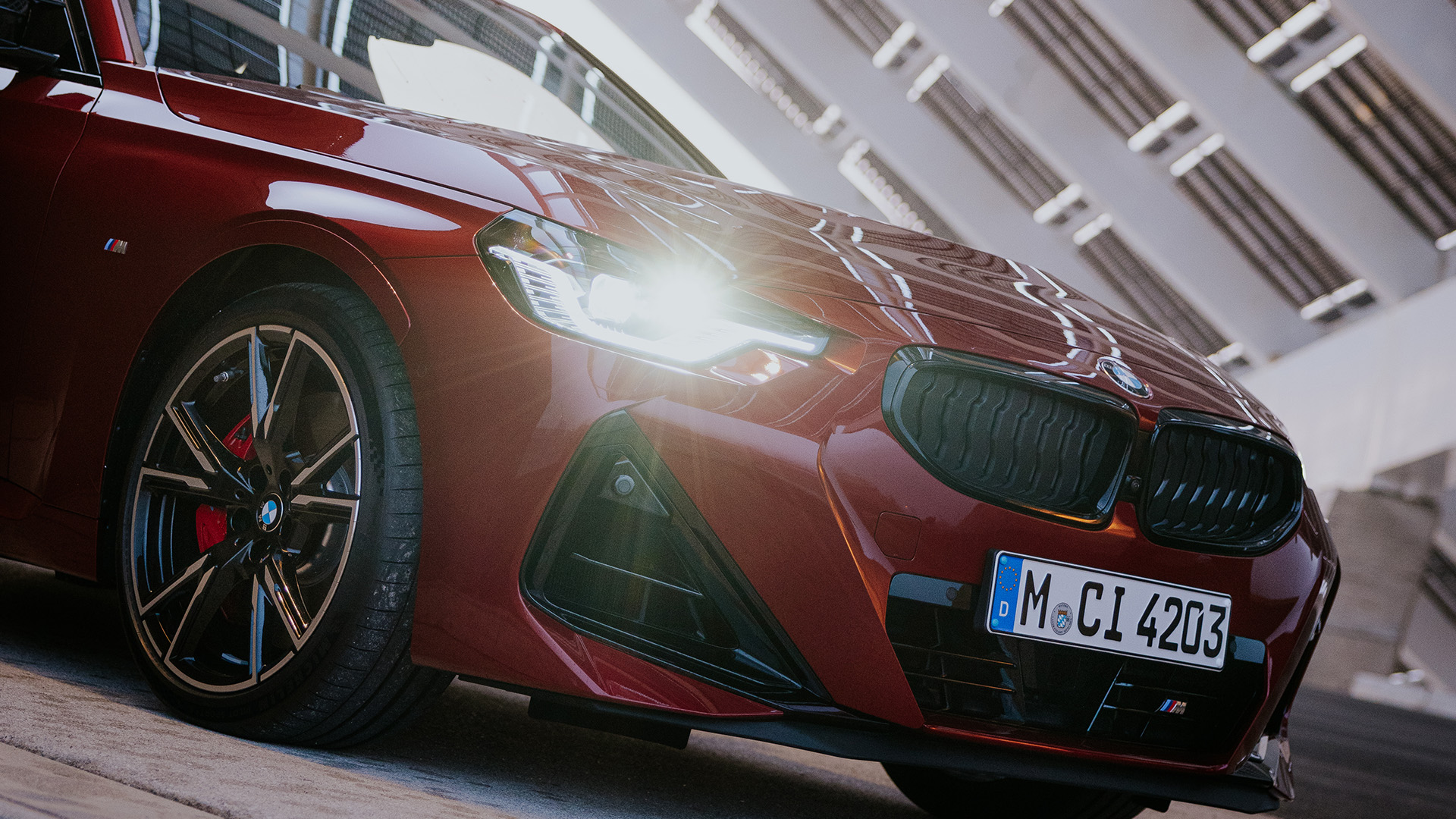 A red BMW car parked on a concrete surface, with a modern architectural structure in the background.
