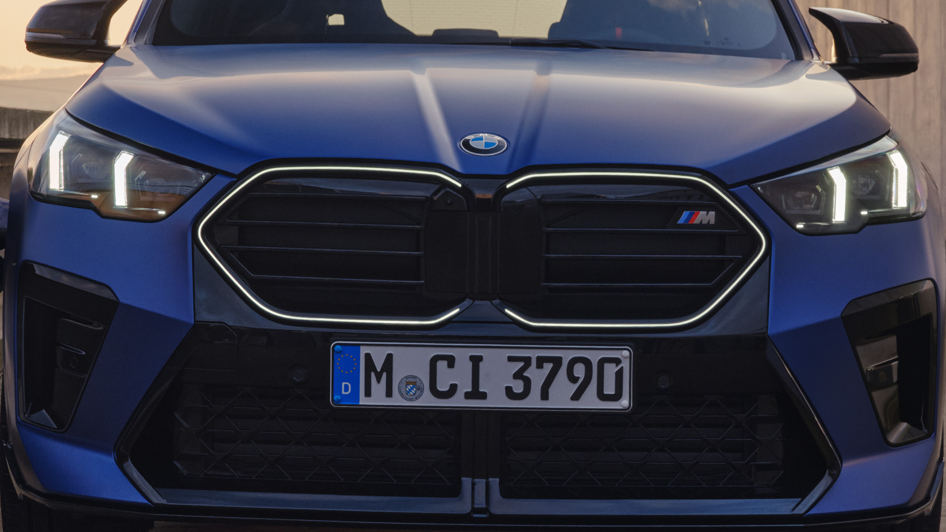 Front view of a blue BMW car showing the grille with illuminated headlights.