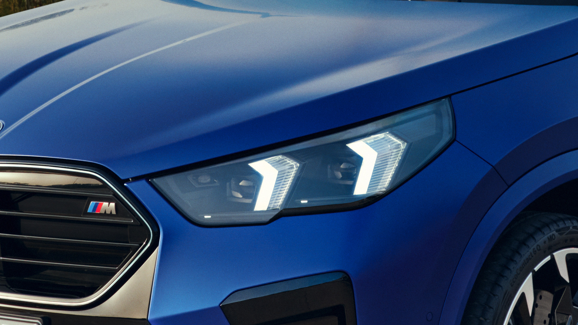 Close-up of the front left headlight and grille of a blue BMW SUV with illuminated LED lights.