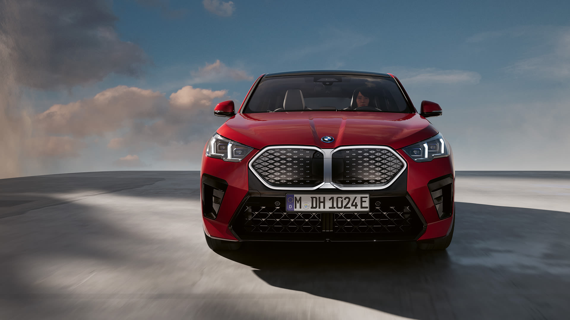 Front view of a red BMW iX2 parked on a open space with light clouds in the sky