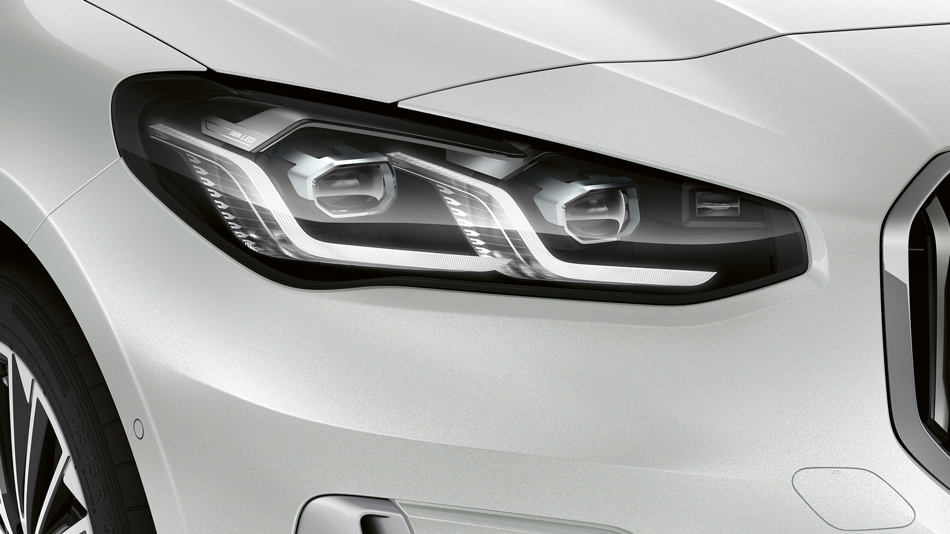 Close-up of the front left headlight and part of the front bumper of a white BMW car, showcasing the modern design and detailing.
