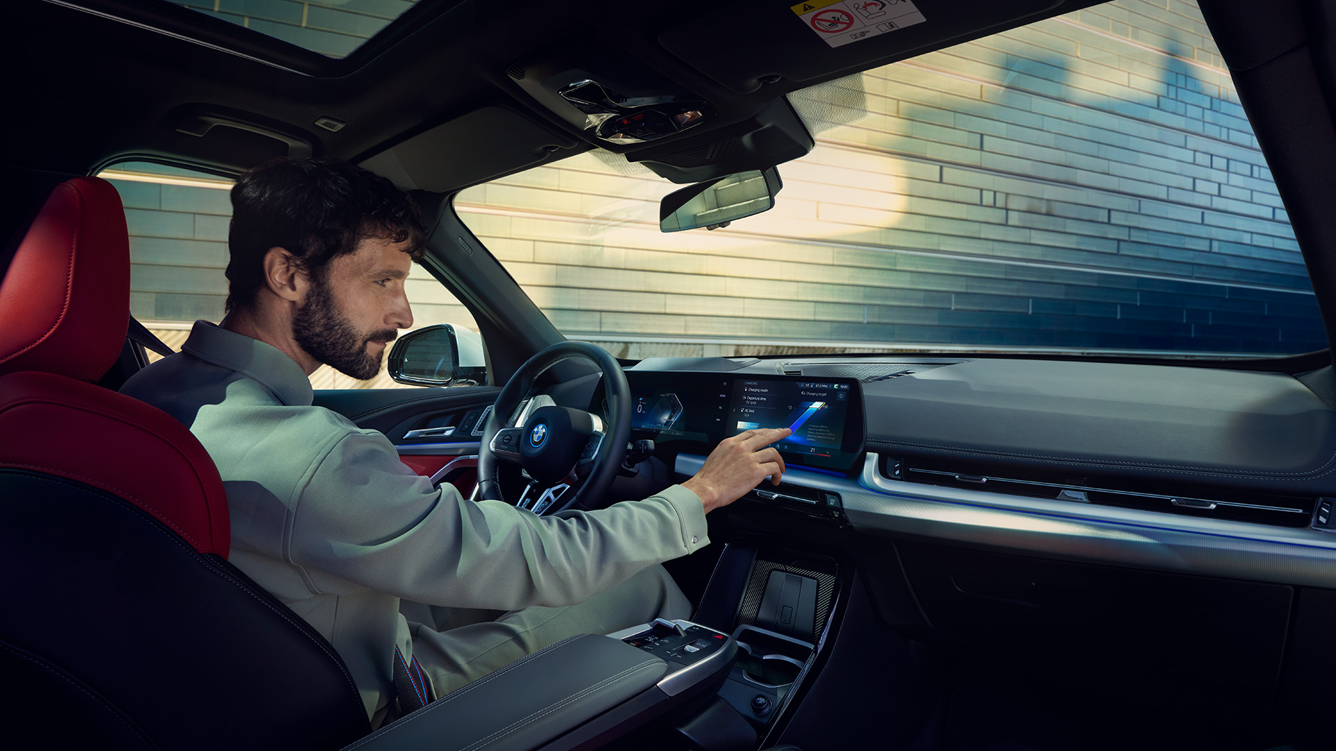 Interior view of a modern BMW car with a person in the driver's seat interacting with the touchscreen display on the dashboard.