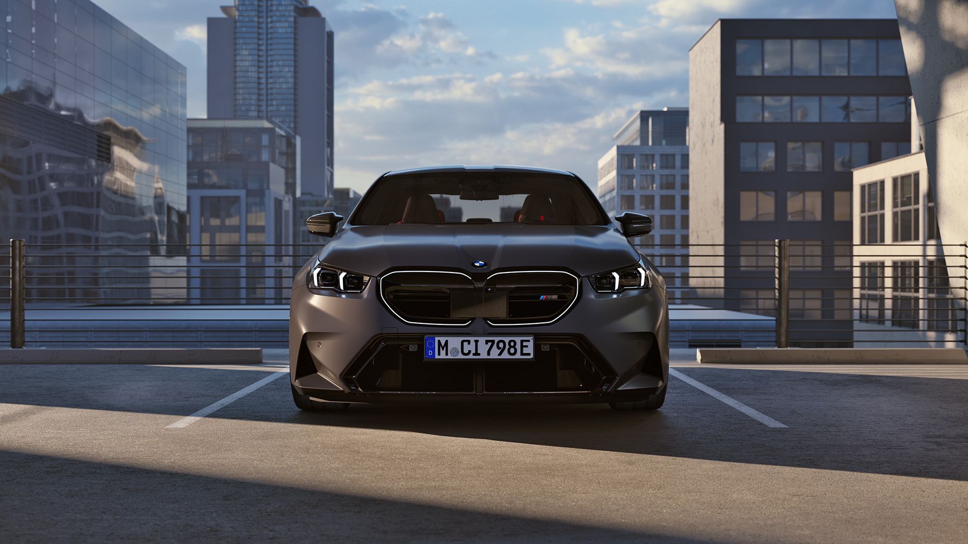 Front view of a BMW car parked in an urban rooftop parking lot with modern buildings and a blue sky in the background.