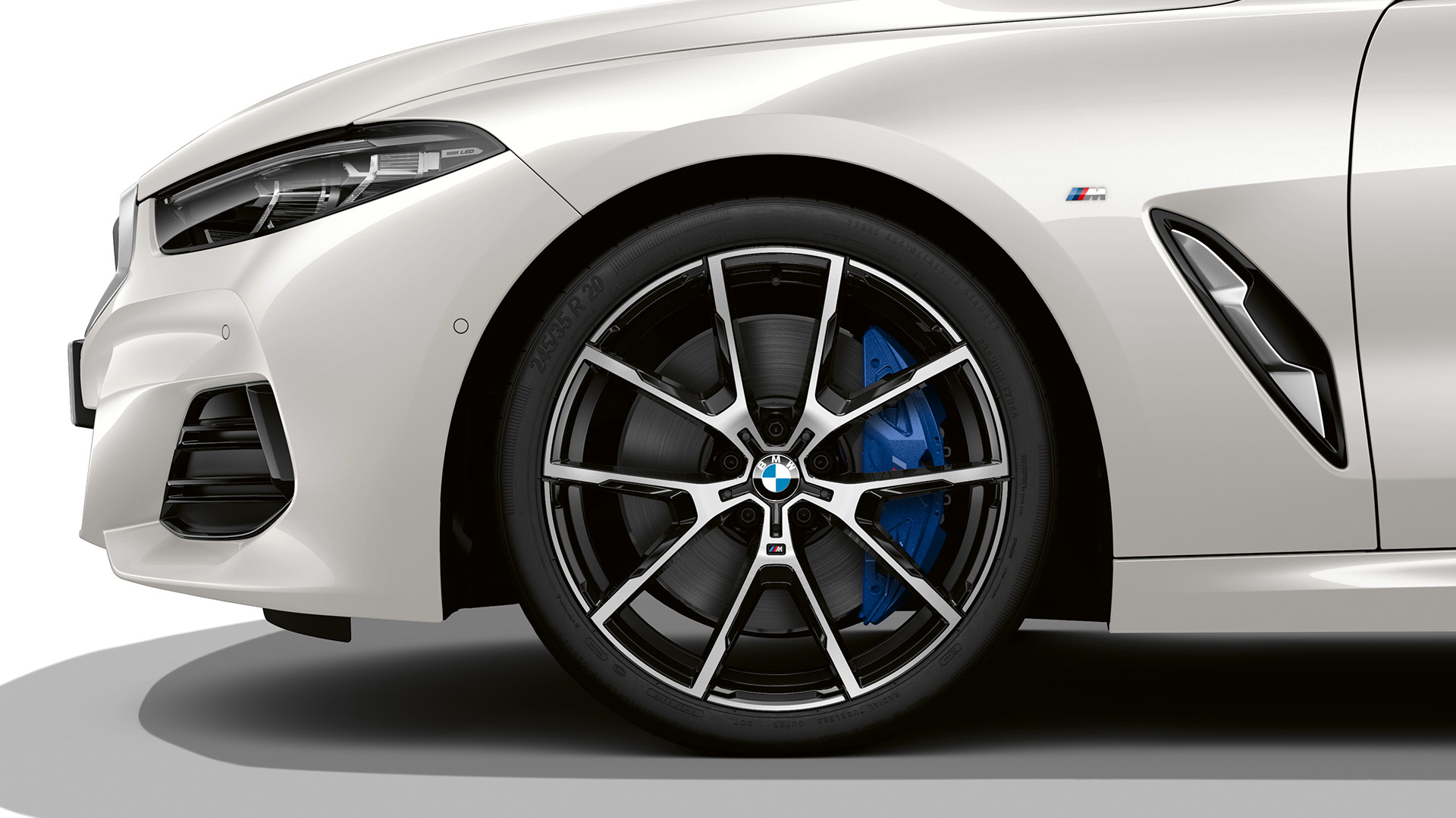 Front side view of a white BMW car showing the front wheel, headlight, and part of the front bumper.