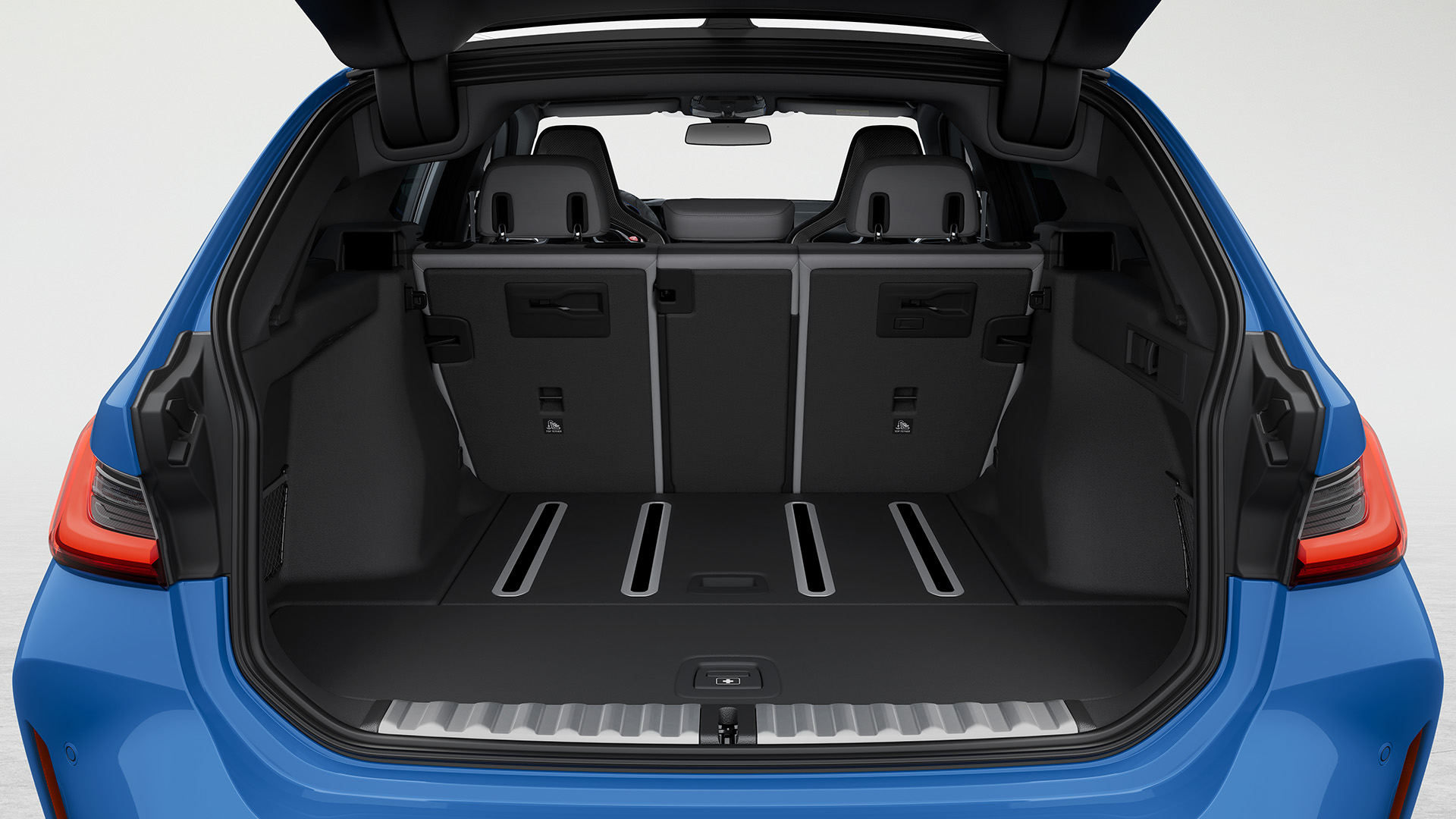 Open trunk of a blue BMW M3 Touring showing spacious cargo area.