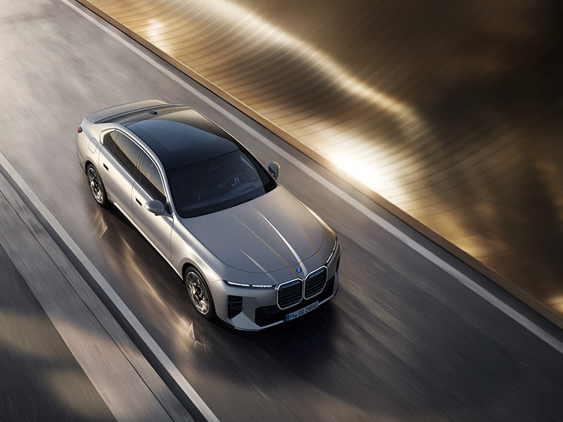 BMW i7 Saloon viewed from above driving along a road beside a curved metallic wall with motion blur.