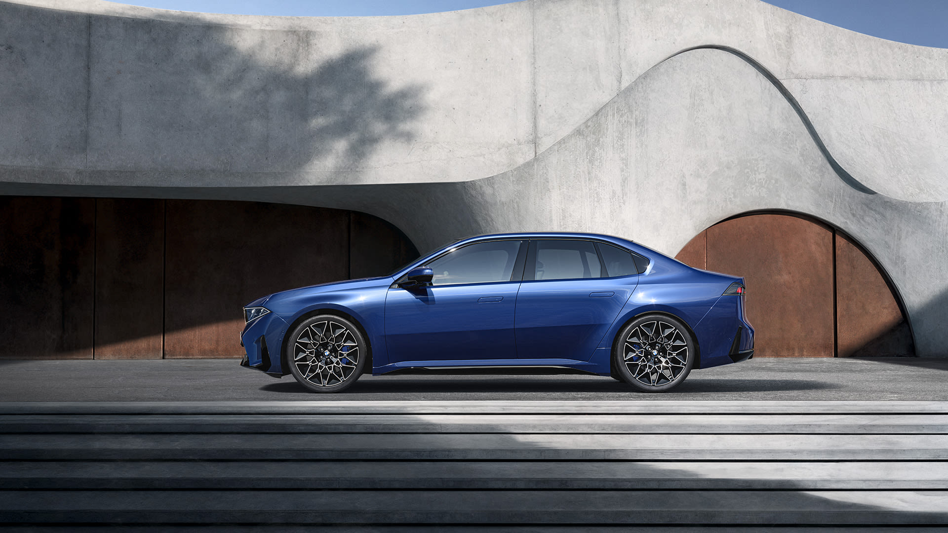 Side view of a blue BMW i3 parked on a raised platform in front of a modern stile building