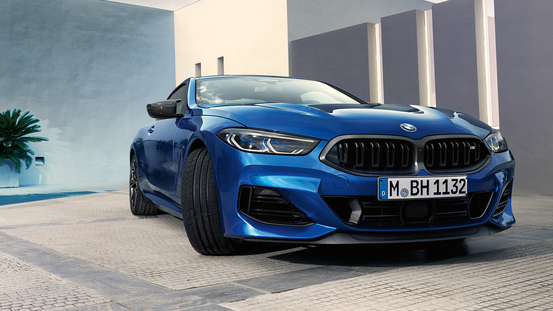 A blue BMW car parked in front of a modern building and a cloudy sky in the background.
