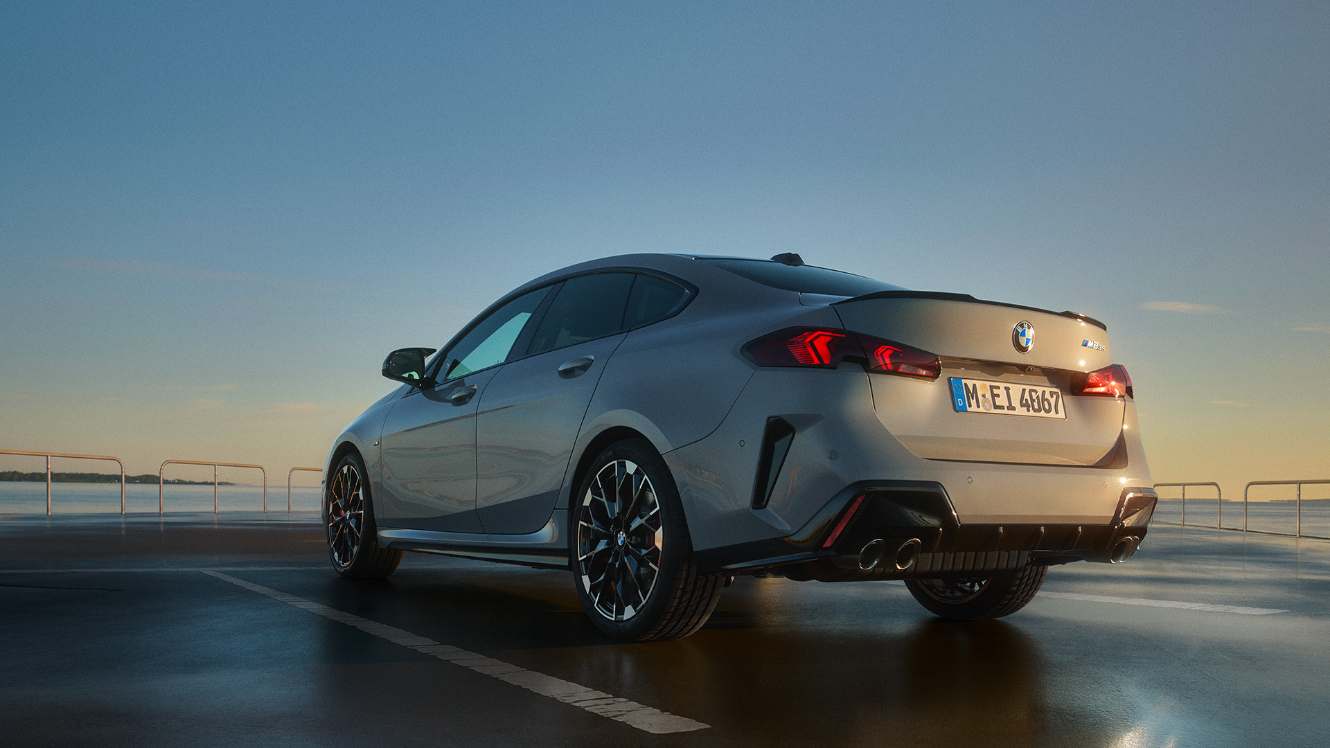 A silver BMW car parked on a wet surface at sunset with a clear sky in the background.