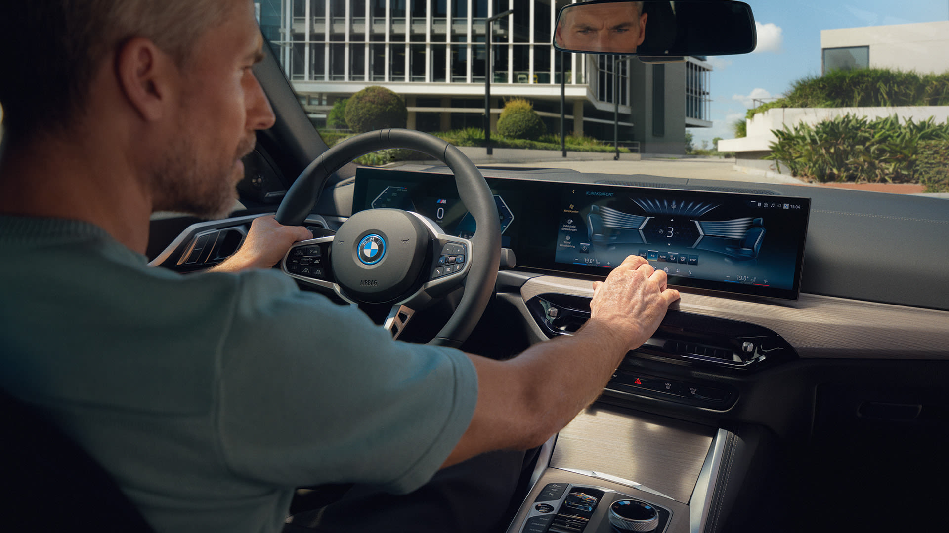 Interior view of person driving on winding road, dashboard and GPS screen visible, with greenery in background.