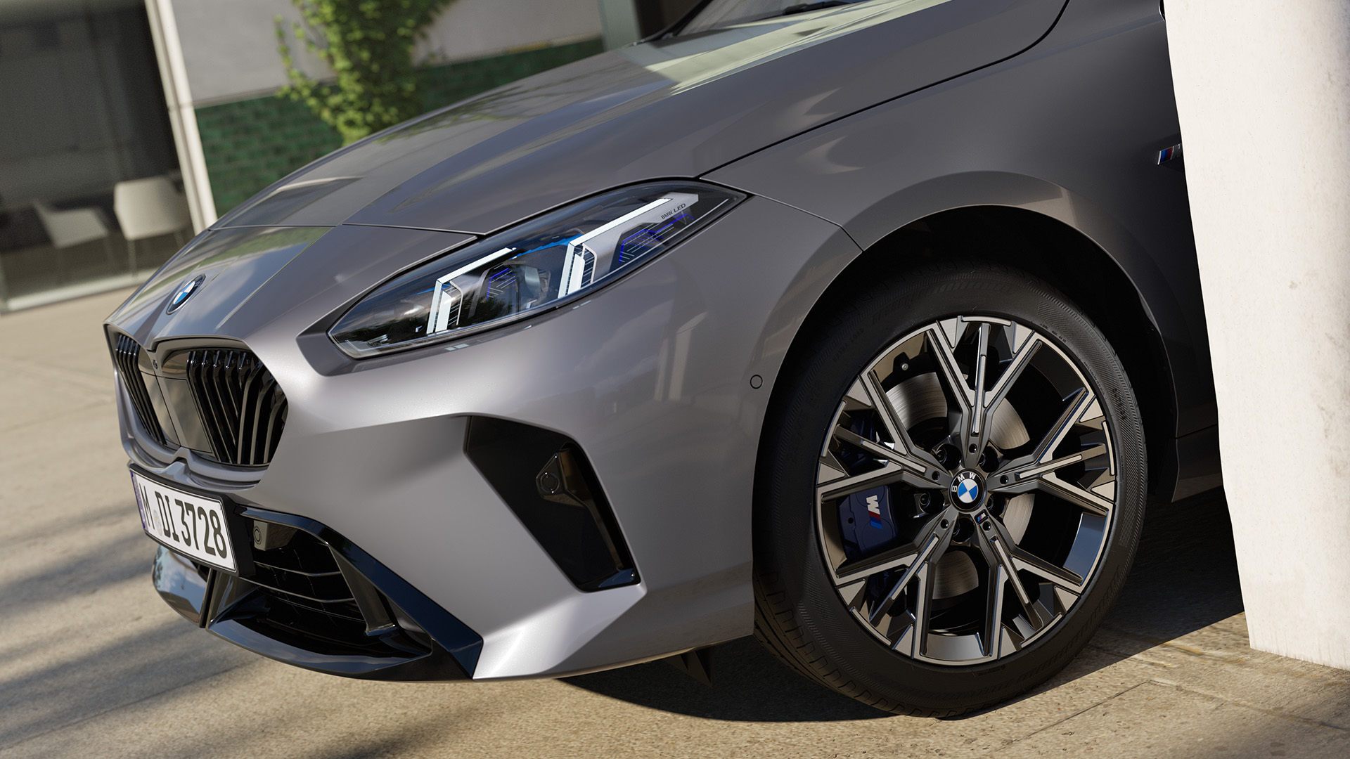 Close-up of a silver BMW car showing the headlight, front grille, and alloy wheel, parked beside a white wall.