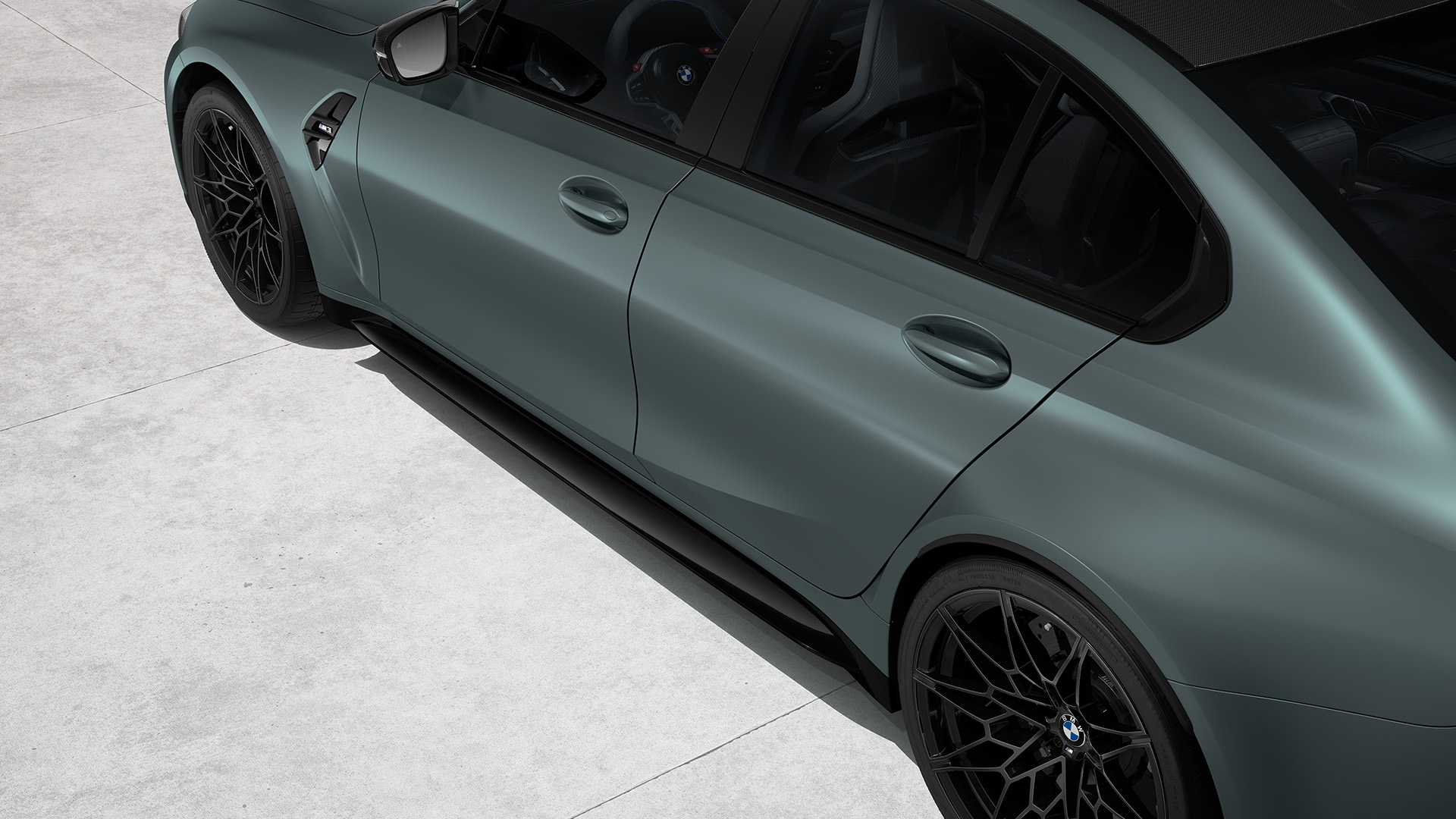 Top view of a matte blue BMW saloon with black rims and a carbon fiber roof, parked on a concrete surface.