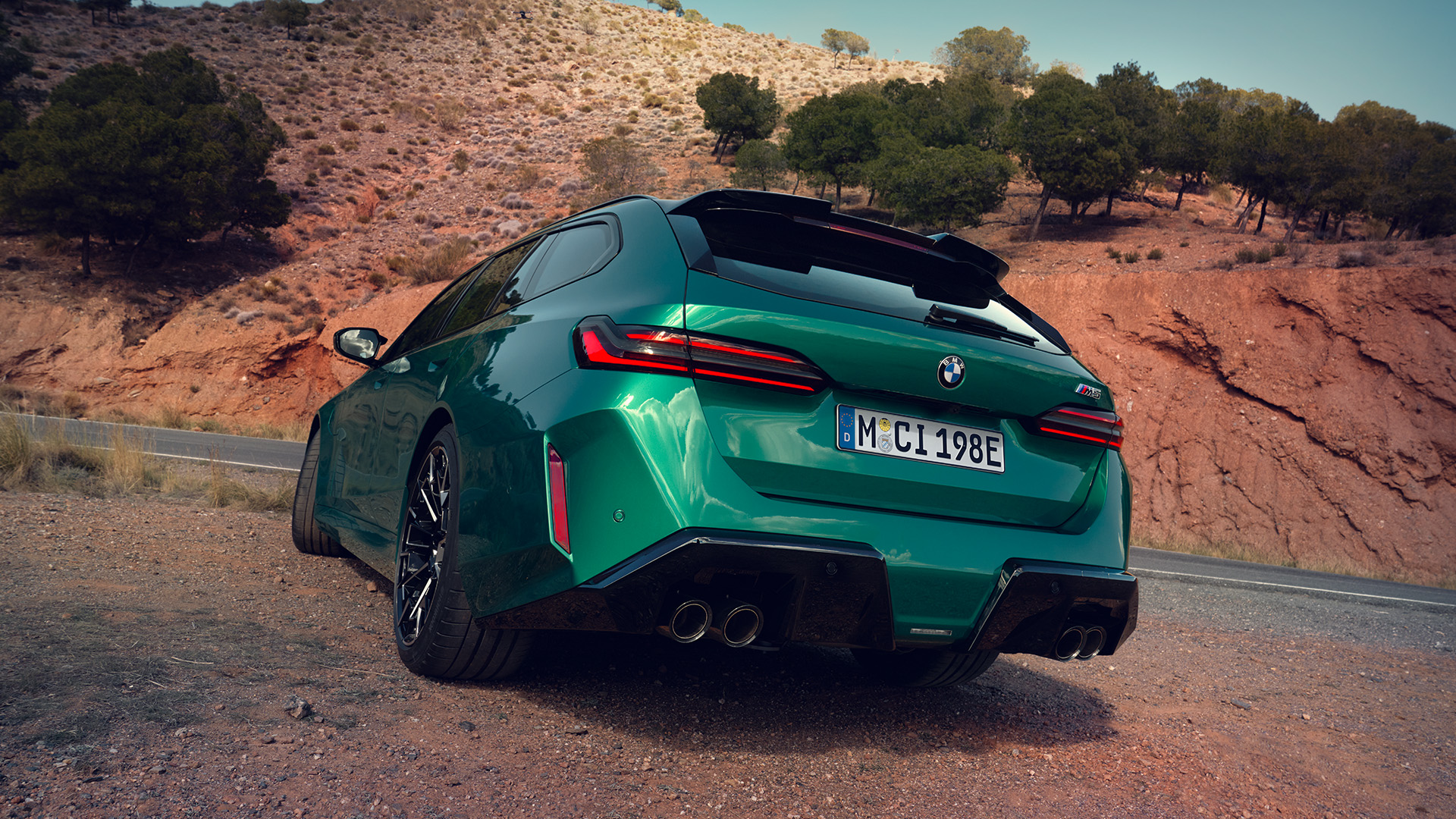 Green BMW car parked on a gravel road with a scenic background of hills and trees.