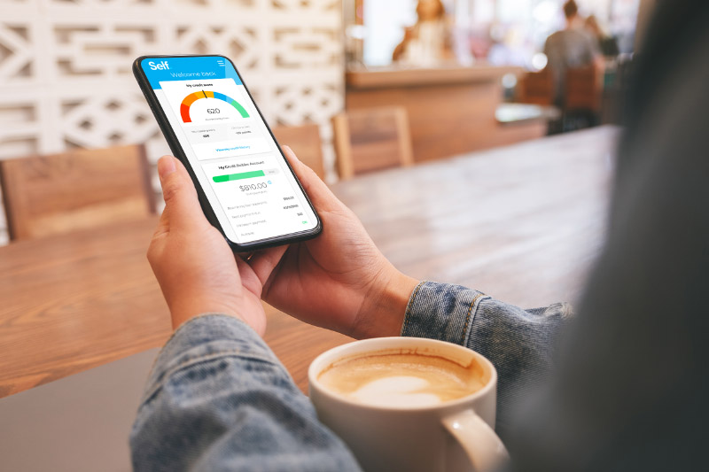 Close up of someone holding a phone with the Self app open on it and a cup of coffee on the table. 