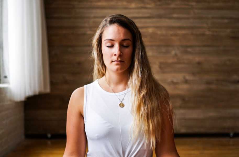 woman sitting indoors cross legged meditating in lotus position 