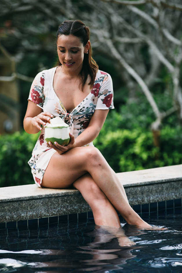 Alba in floral dress with a coconut and feet in the pool