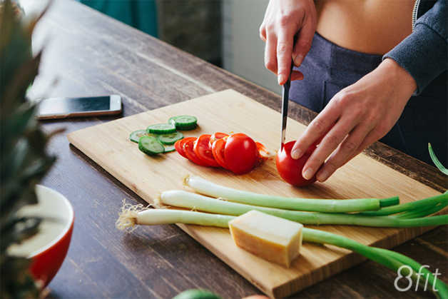 Tomatoes being chopped on cutting board with cucumbers 