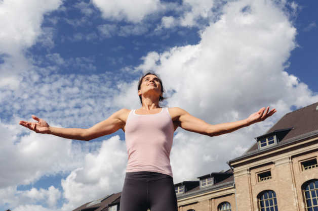 Ame outside. arms outstretched, with clouds and blue sky in the background 