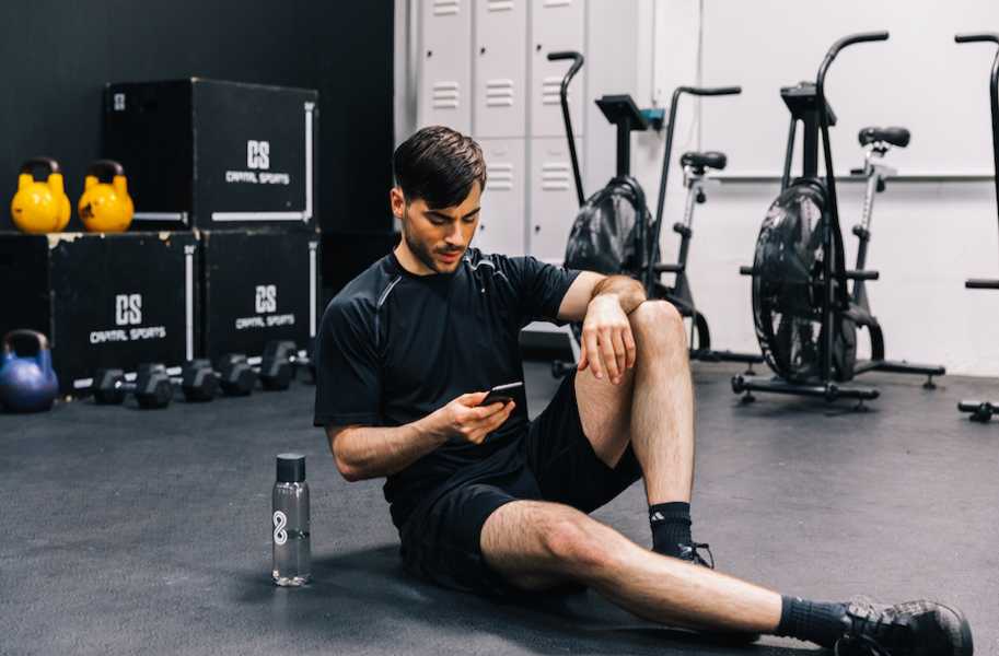 Man sitting with phone at the gym, next to 8fit bottle