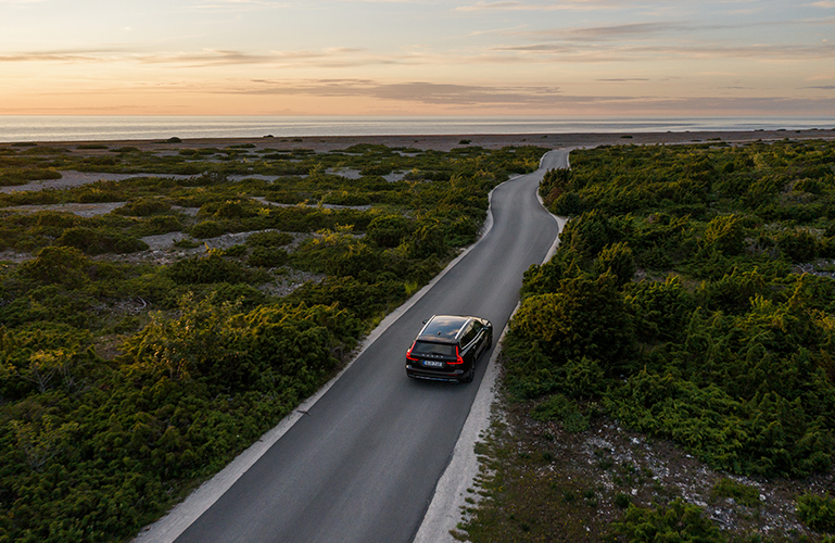 Volvobil som kör längs en kustväg i solnedgången
