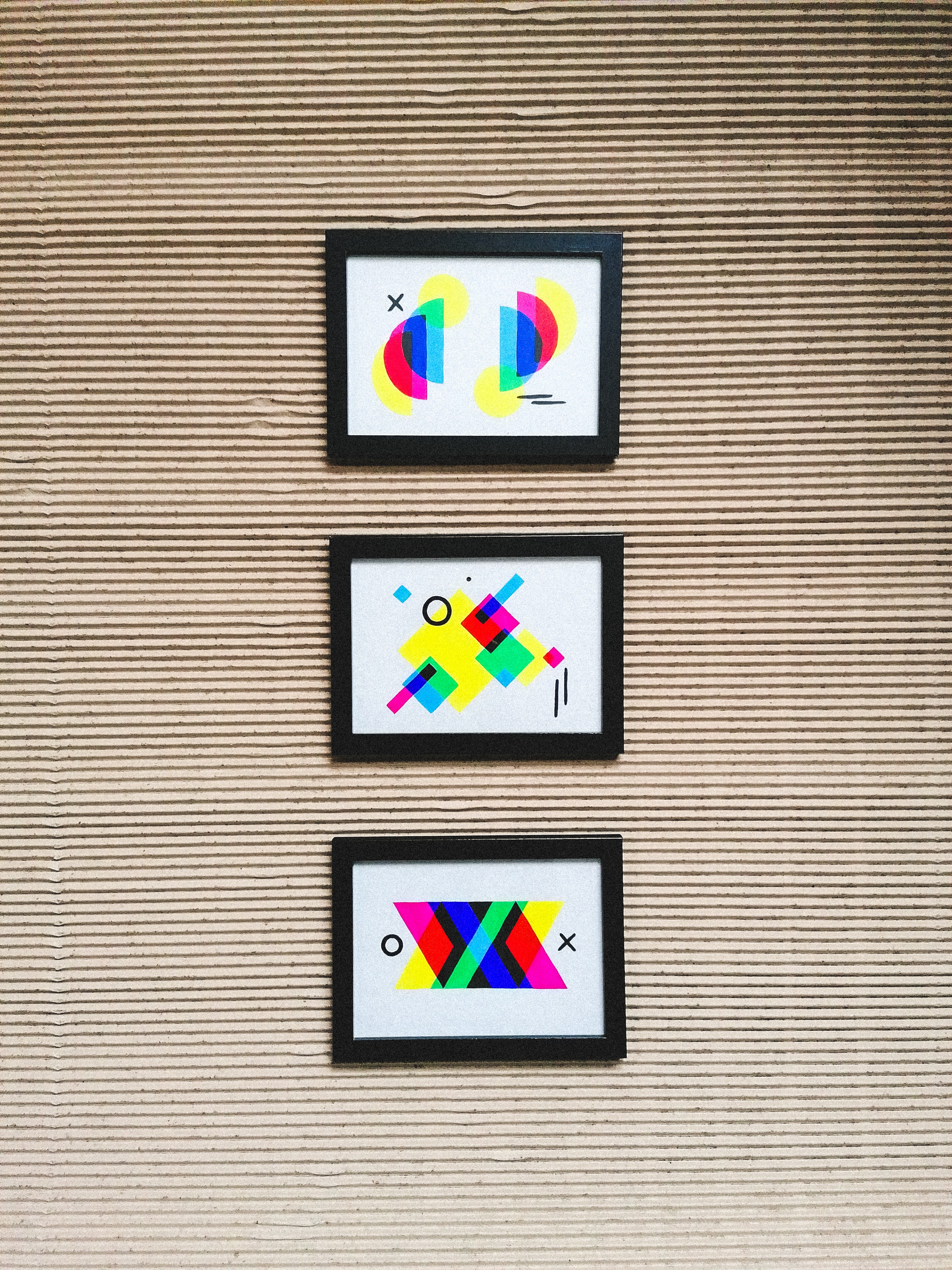 Three brightly colored, framed geometric prints hanging on a wall