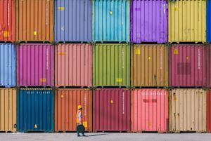 Worker in high-visibility vest walking past a wall of colorful stacked shipping containers