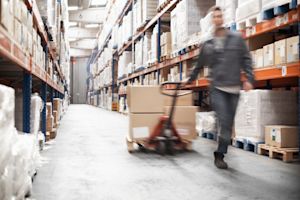 Warehouse associate pulling a pallet jack of boxes down an aisle of tall racks