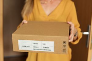 Woman holding a labeled shipping box at her front door