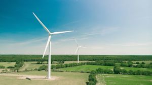 Two wind turbines on a green farmland landscape under a blue sky with distant turbines on the horizon