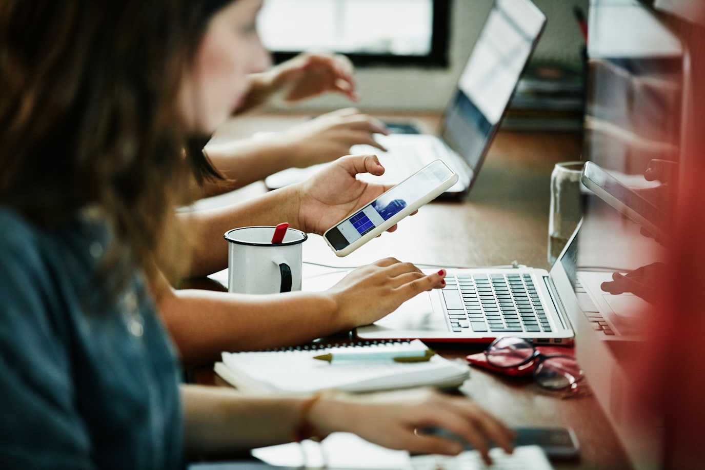 Person staring at phone while working on laptop