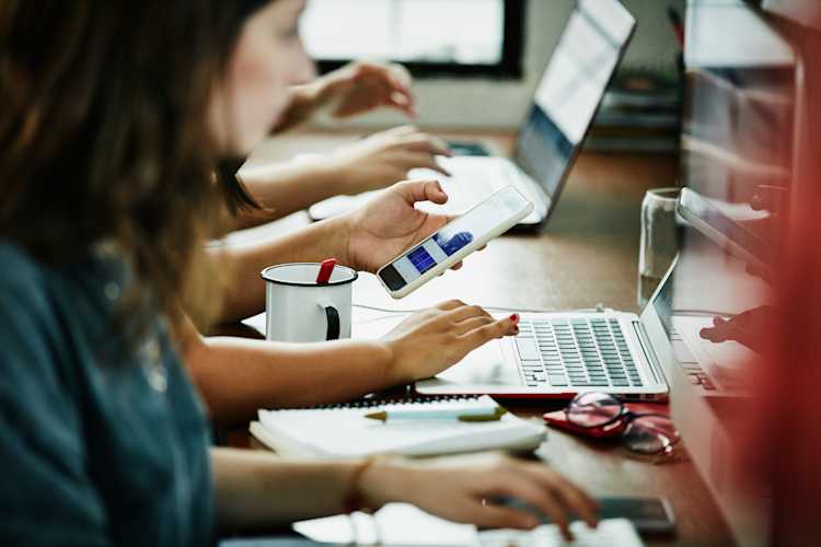 Person staring at phone while working on laptop