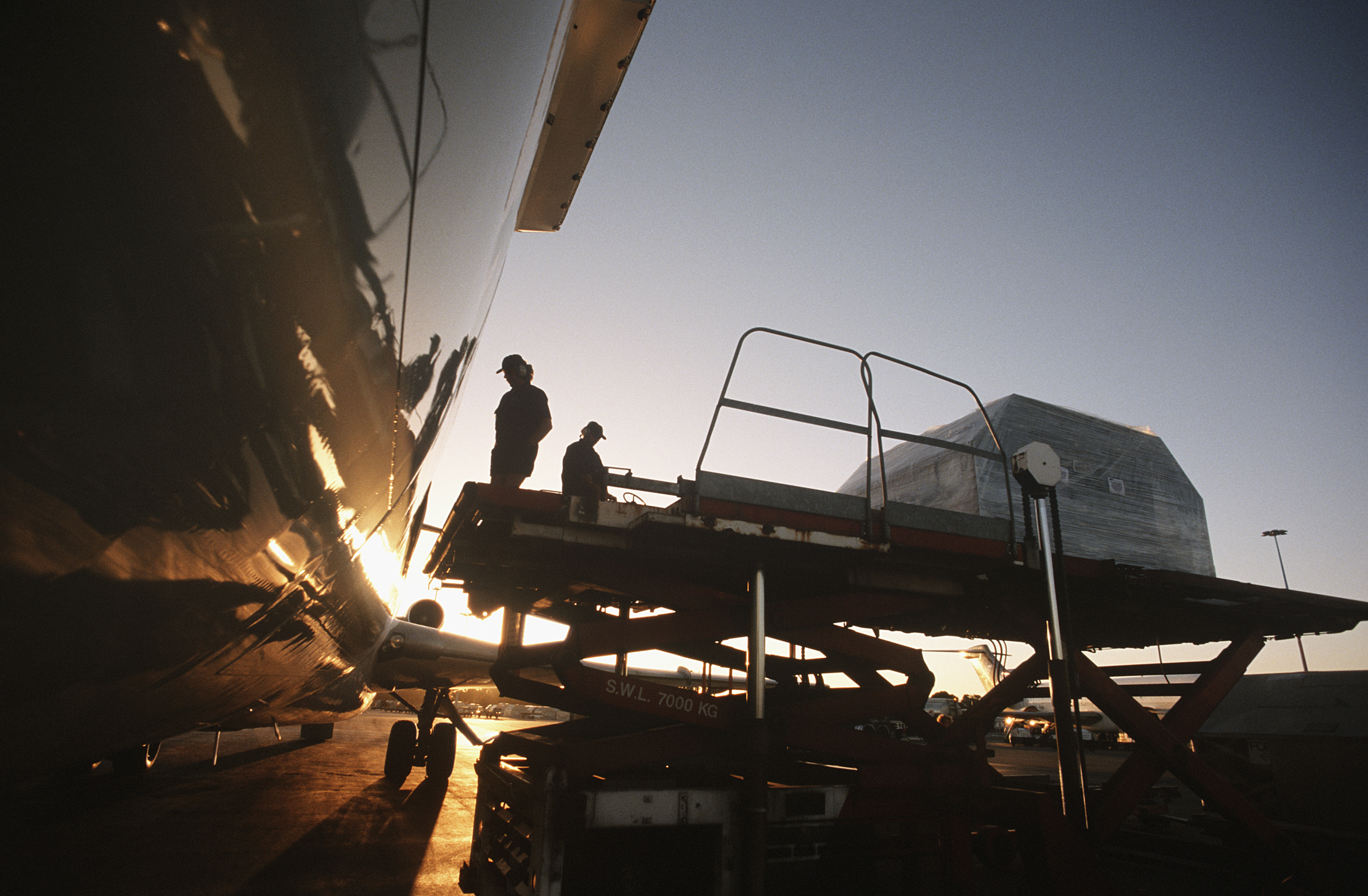 Ground crew loading air cargo onto a freighter aircraft at sunset