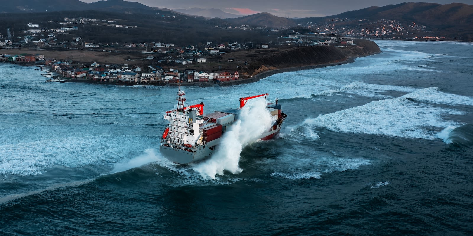 Container ship heading into port during a storm signifying uncertainty and risks in the outlook for the economy and logistics industry.