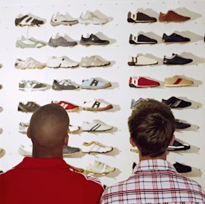 Two shoppers browsing a wall display of sneakers and athletic shoes in a retail store