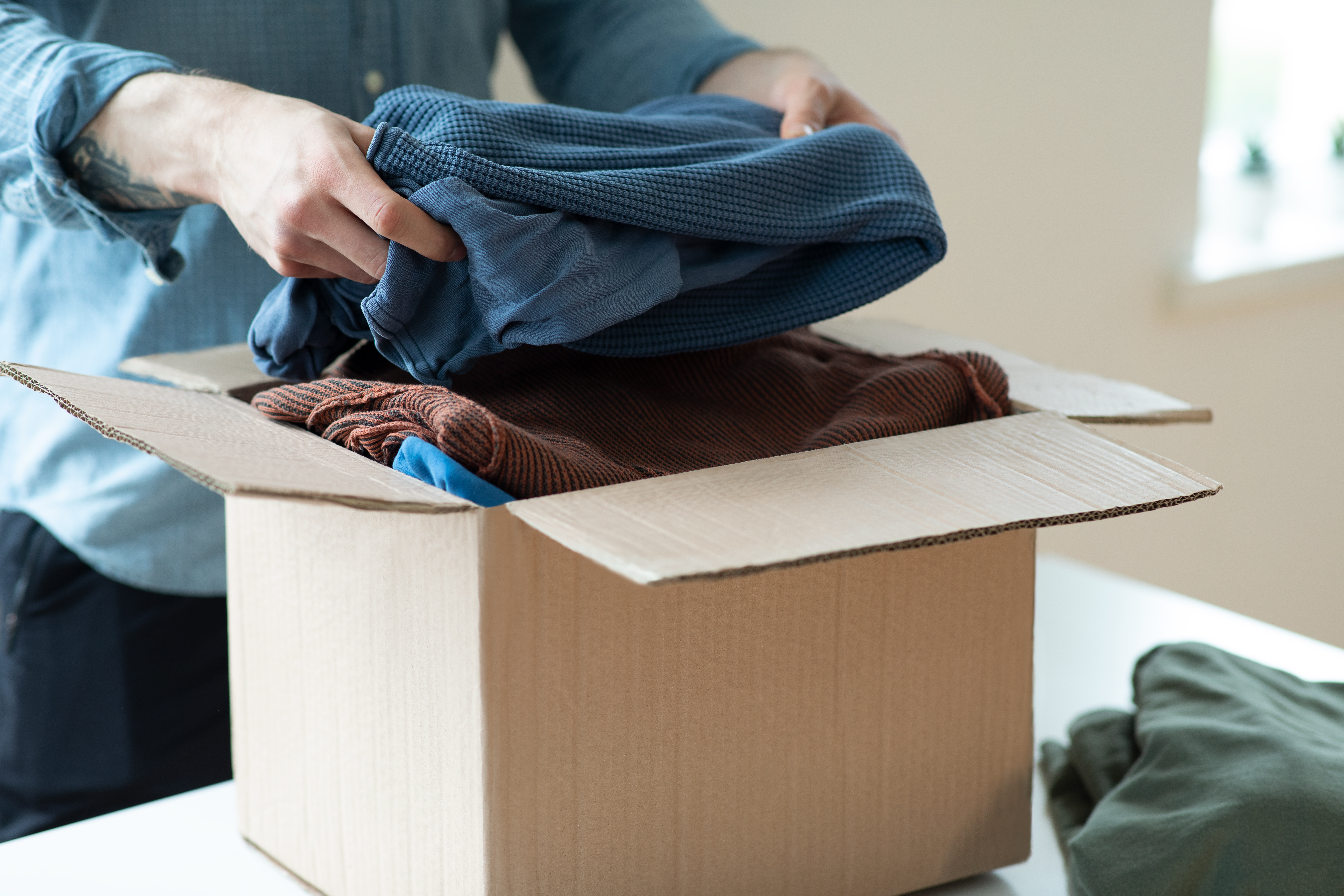 Person folding and packing clothing into a cardboard shipping box