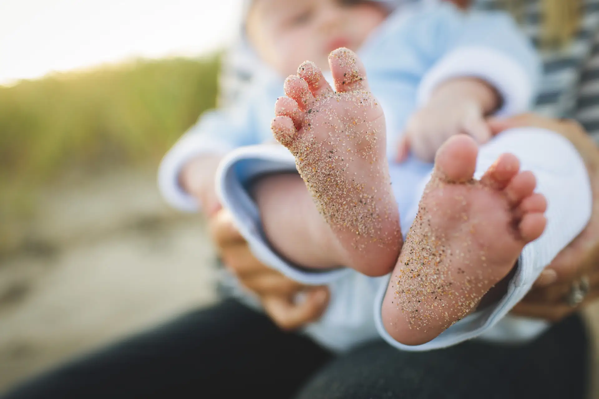 A child being held with sand on its feet