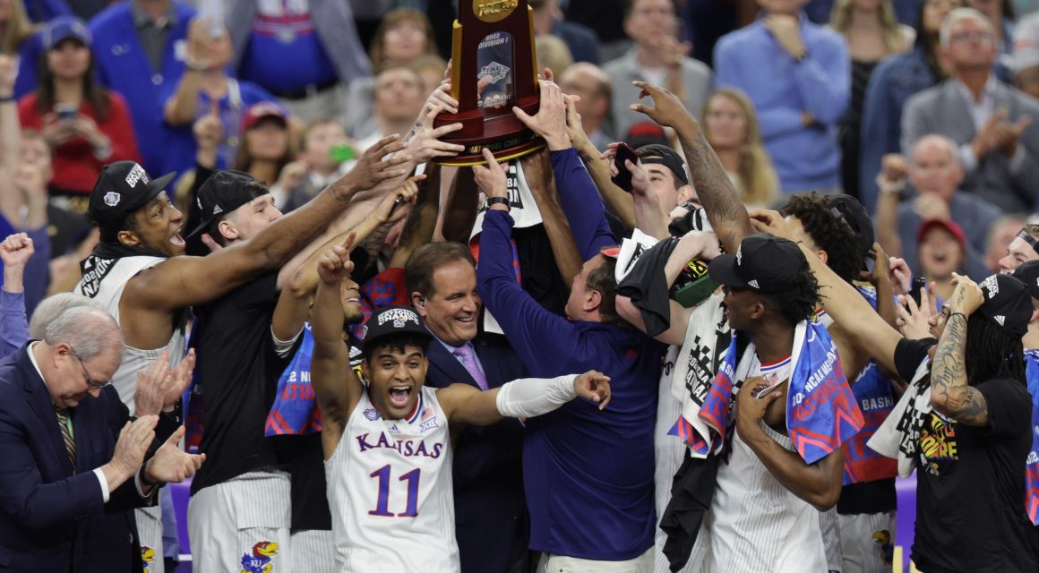 Kansas Jayhawks guard Remy Martin (11) celebrates as head coach Bill Self (middle right) helps lift the championship trophy after defeating the North Carolina Tar Heels during the 2022 NCAA men's basketball tournament Final Four championship game at Caesars Superdome. Mandatory Credit: Stephen Lew-USA TODAY Sports.