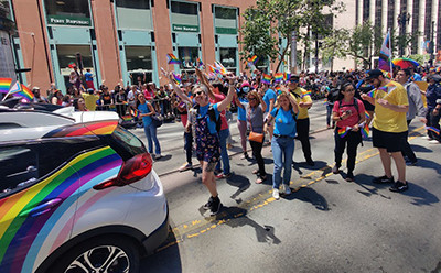 Rainbow wrapped cruise car and people walking in pride parade