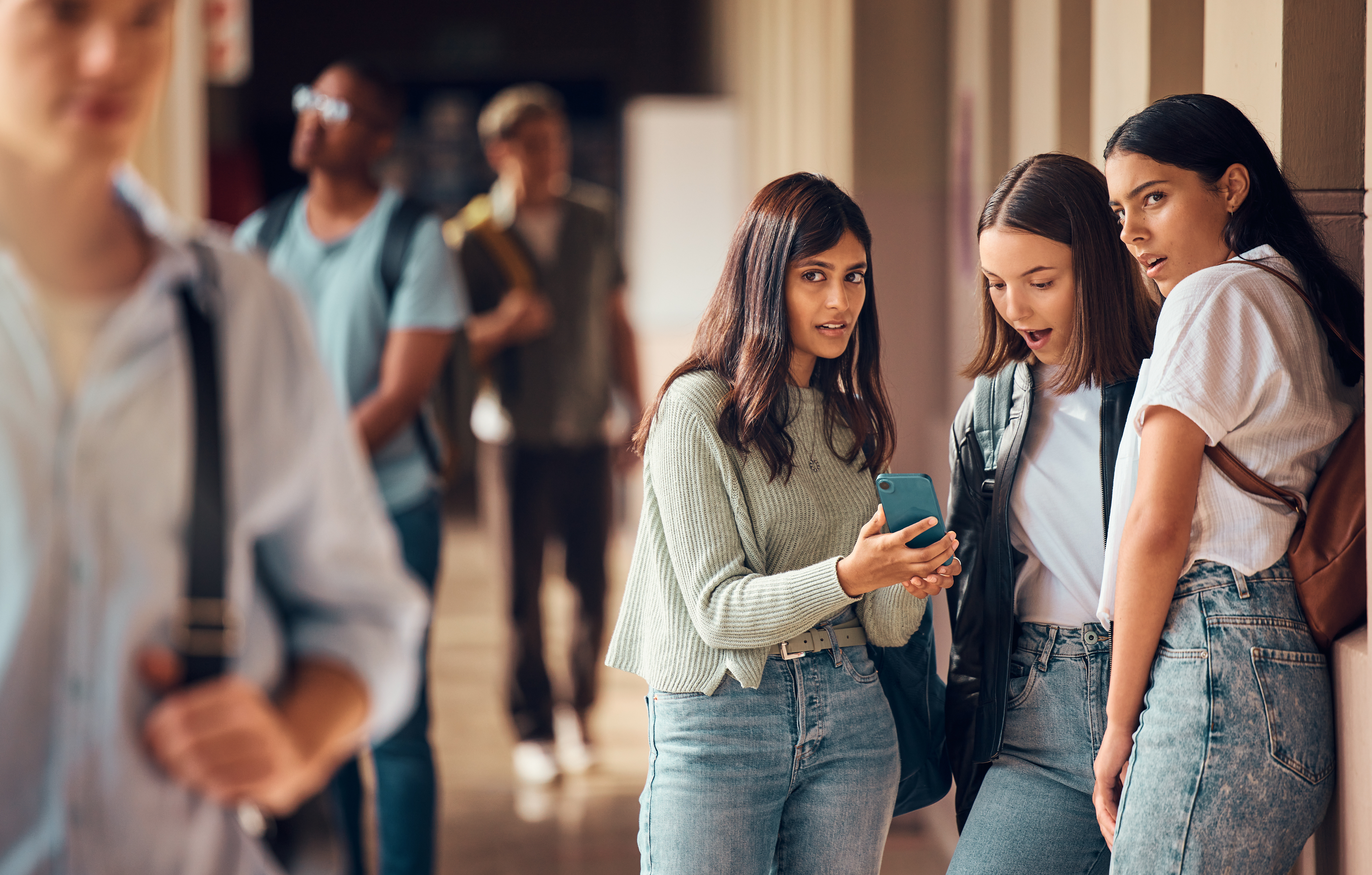 Students in school hallway looking at phone containing cyberbullying content