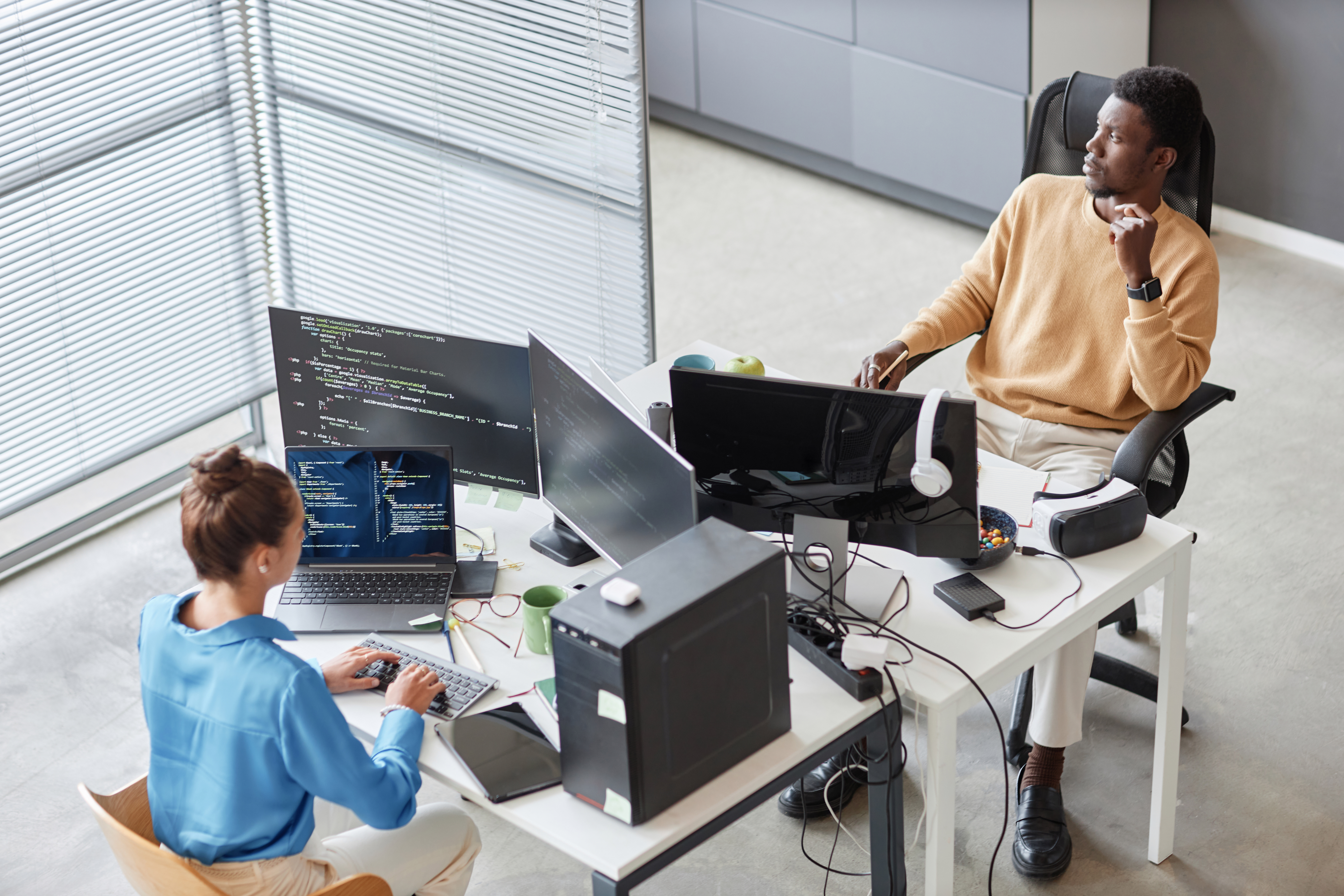 Man looking out window while woman write code on computer