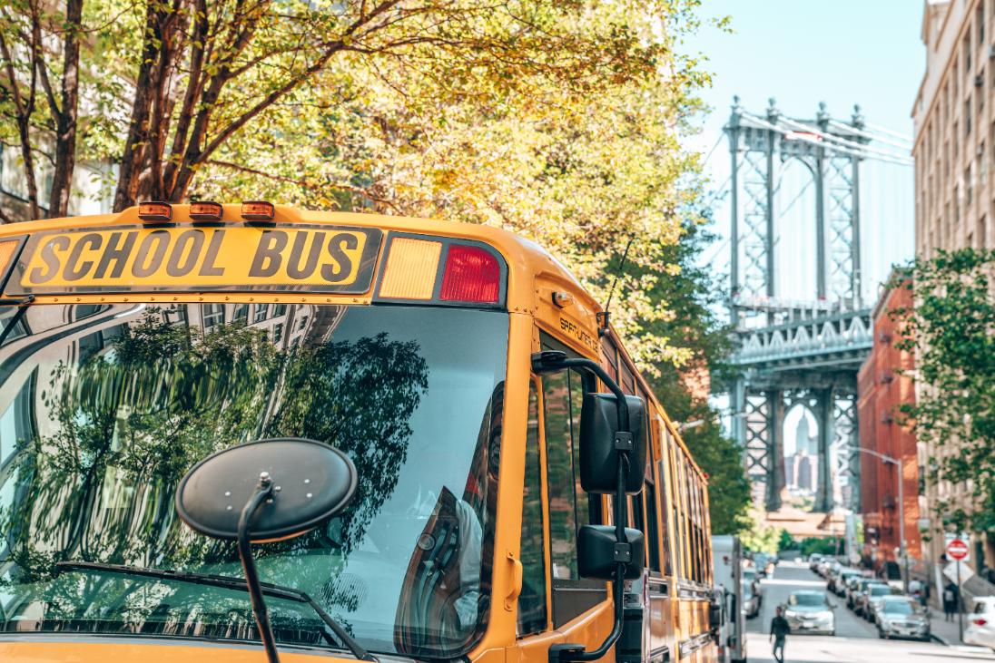 Image of a yellow school bus in the foreground of the Brooklyn Bridge